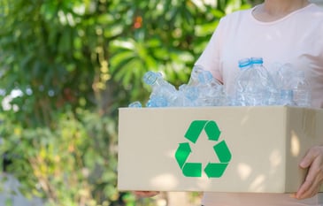 persona sosteniendo una caja de cartón que contiene reciclaje de plástico